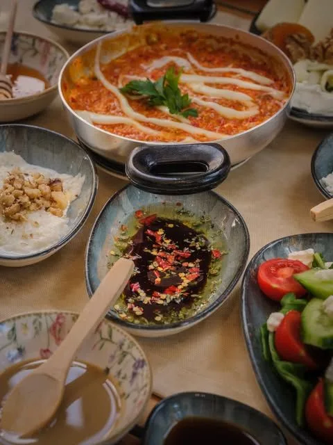 Yoğurtlu sıcak domates soslu yemek, salata ve küçük kaselerle dolu masa