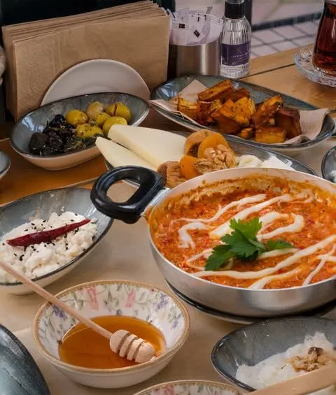 Tavada sıcak domatesli yemek, yanında bal, zeytin ve peynir tabakları
